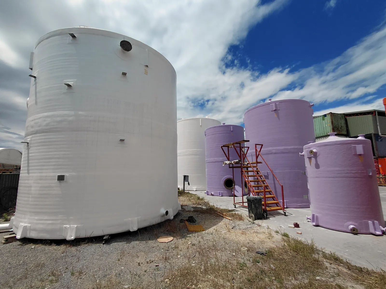A large white FRP tank with vertical FRP chemical tanks behind it
